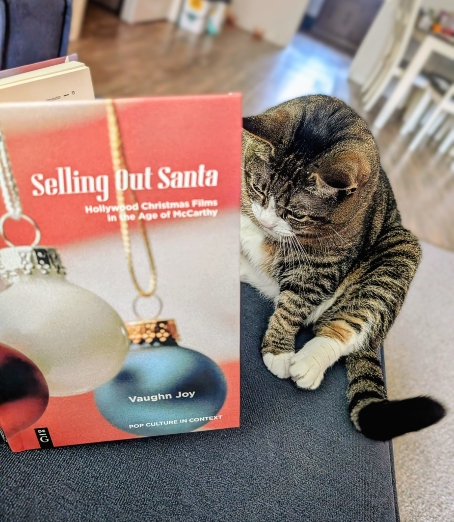 Biscuits sitting like a goblin on her butt reading Selling Out Santa