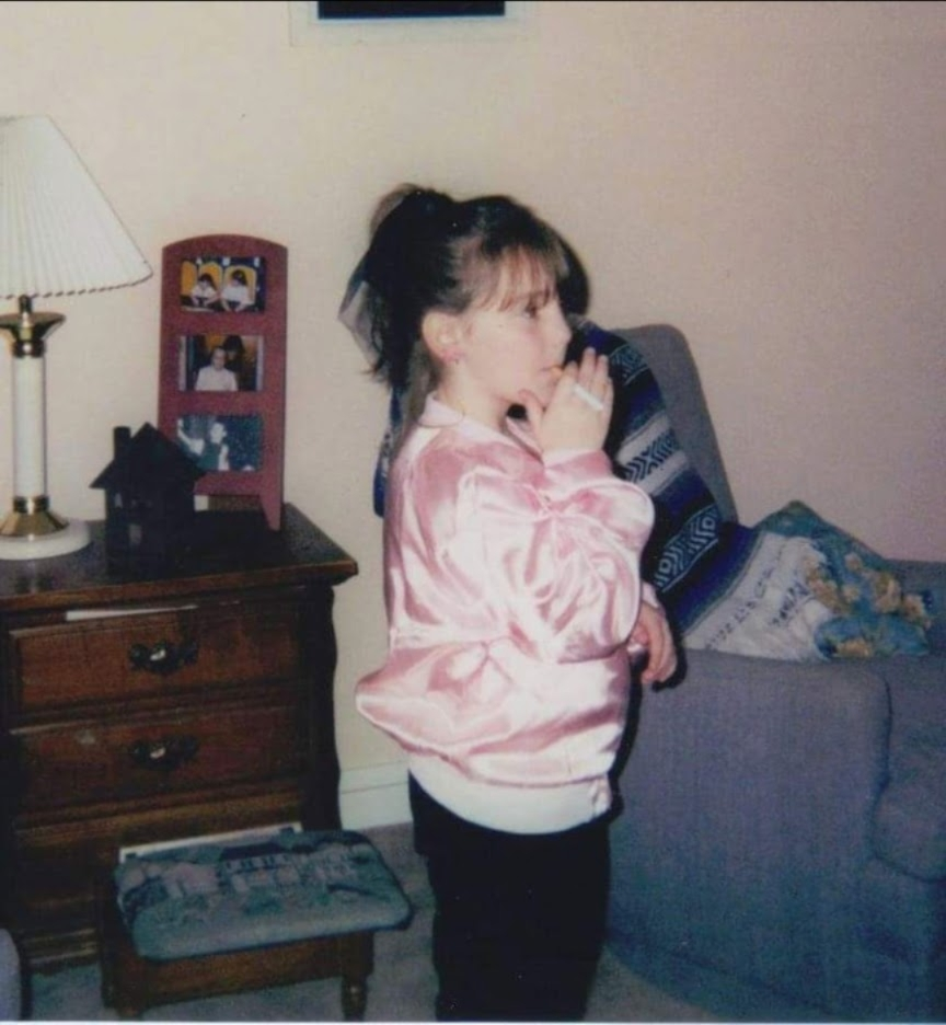 Child me on Halloween dressed as a Pink Lady circa 2001(?) wearing a pink jacket and holding a cigarette in our living room